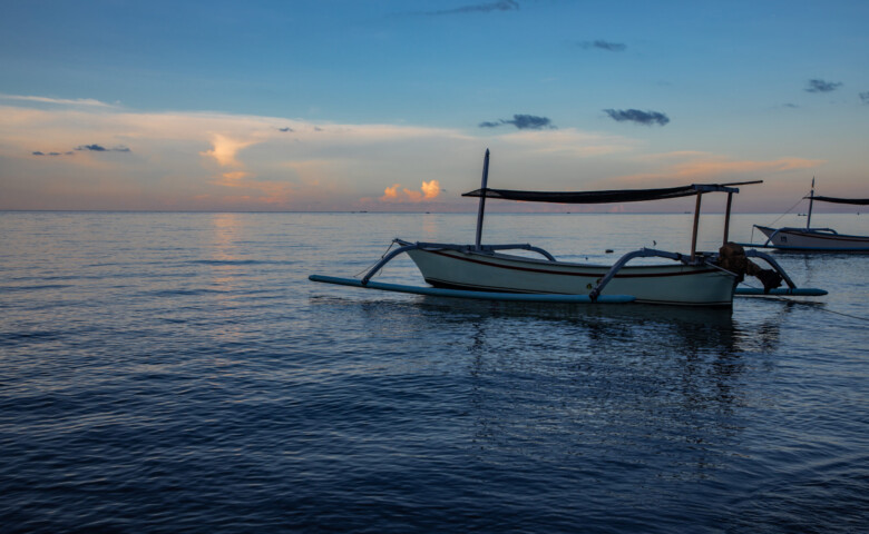 Blue hour over calm ocean and black sand beach with balinese boat