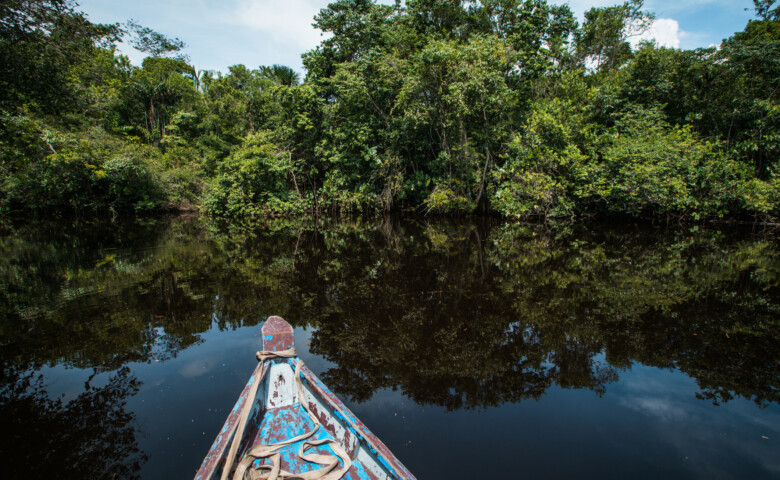 An open wooden boat floating on a brown tropical river, Guyana, South America.