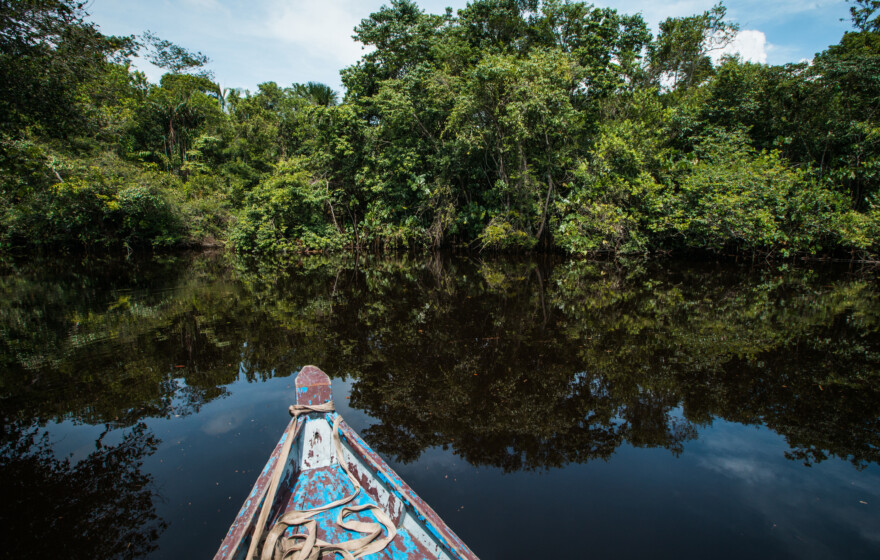 An open wooden boat floating on a brown tropical river, Guyana, South America.