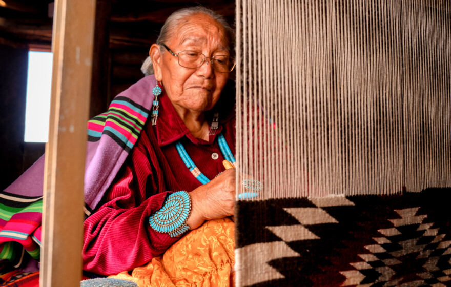 Traditional Navajo elderly woman working on a blanket loom in an authentic hogan